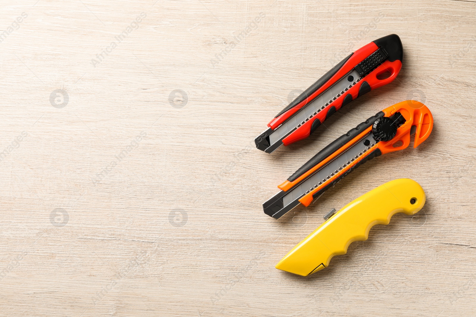 Photo of Different utility knives on white wooden table, flat lay. Space for text