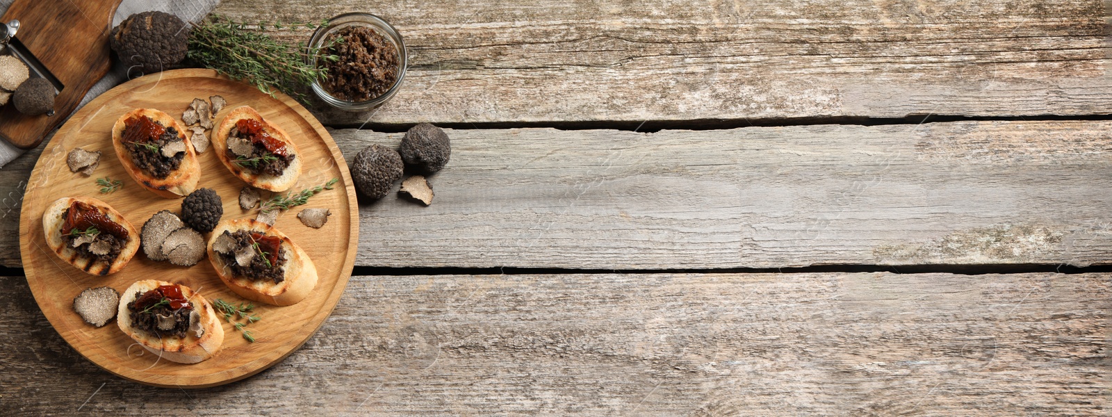 Image of Delicious bruschettas with truffle sauce and dried tomatoes on wooden table, flat lay with space for text. Banner design