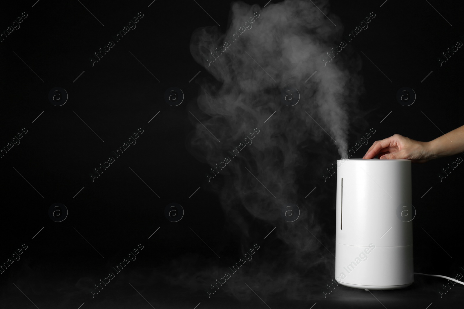 Photo of Woman using modern air humidifier on black background, closeup. Space for text