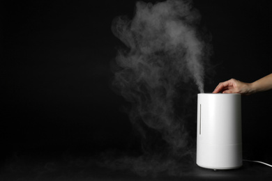 Woman using modern air humidifier on black background, closeup. Space for text