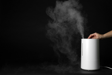 Photo of Woman using modern air humidifier on black background, closeup. Space for text