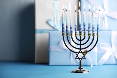Photo of Hanukkah celebration. Menorah with burning candles and gift boxes on light blue table, space for text