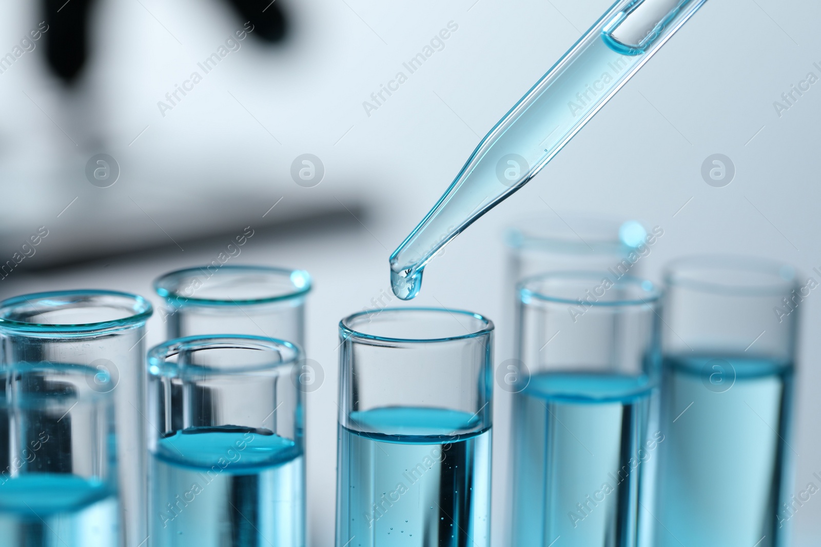 Photo of Dripping liquid from pipette into test tube on blurred background, closeup