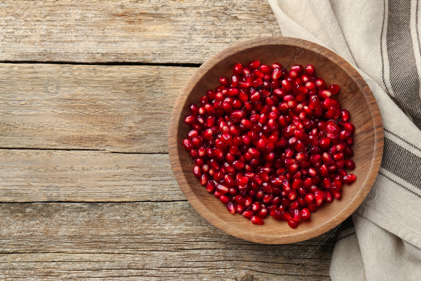 Photo of Ripe juicy pomegranate grains in bowl on wooden table, top view. Space for text