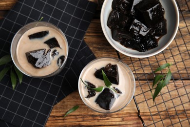 Photo of Glasses of milk with grass jelly on wooden table, flat lay