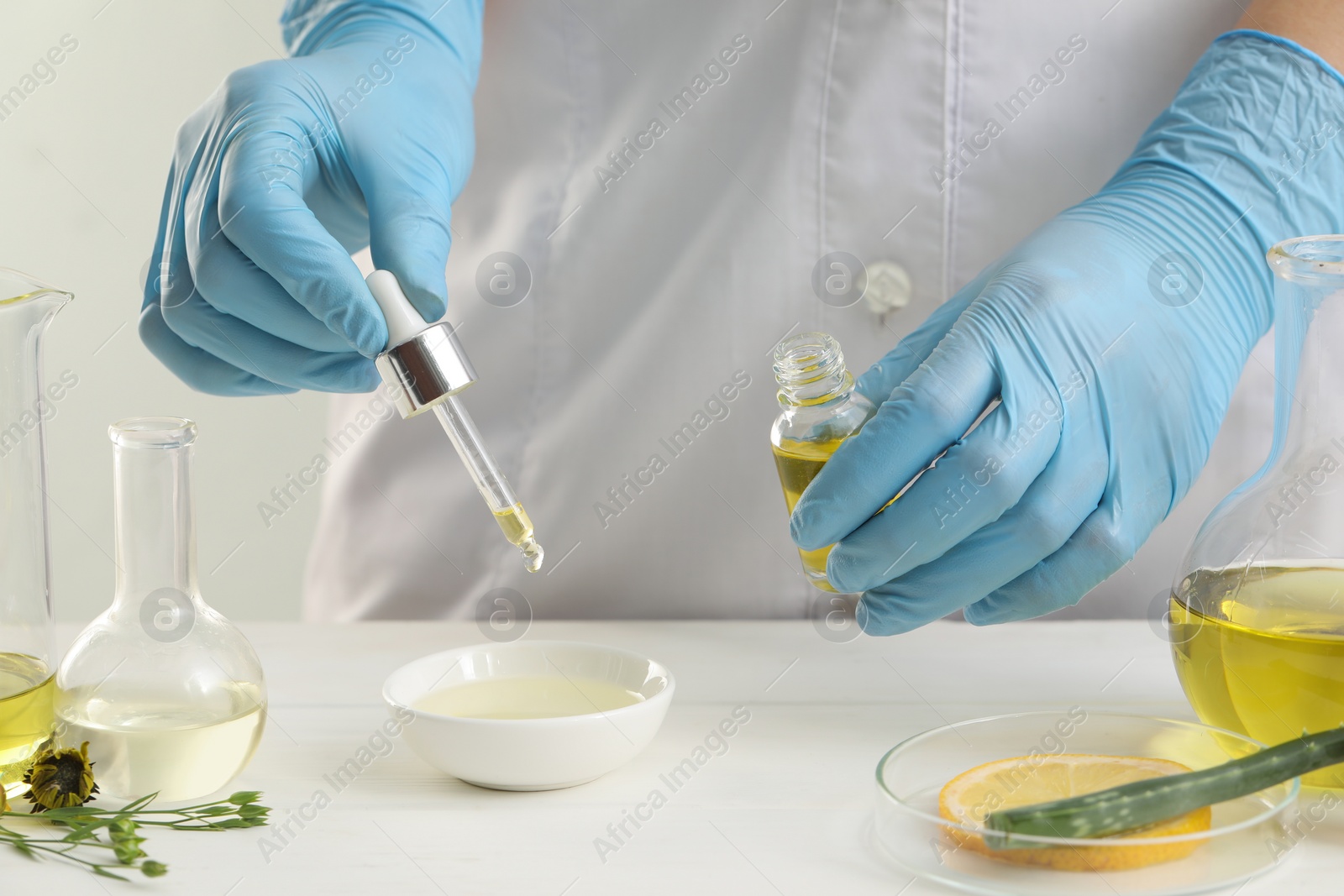 Photo of Scientist developing cosmetic oil at white table, closeup