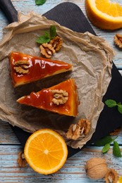 Pieces of delicious caramel cheesecake with walnuts and orange served on wooden table, flat lay