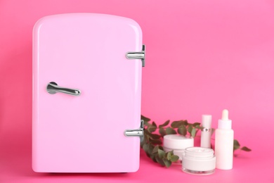 Photo of Cosmetic refrigerator and skin care products on pink background