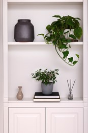 Interior design. Shelves with stylish accessories, potted plants and books near white wall