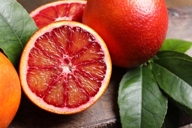Photo of Ripe red oranges and green leaves on wooden table, closeup