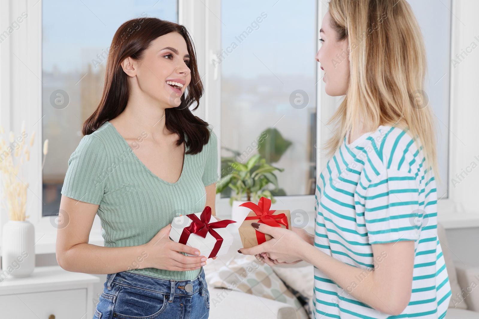 Photo of Smiling young women presenting gifts to each other at home