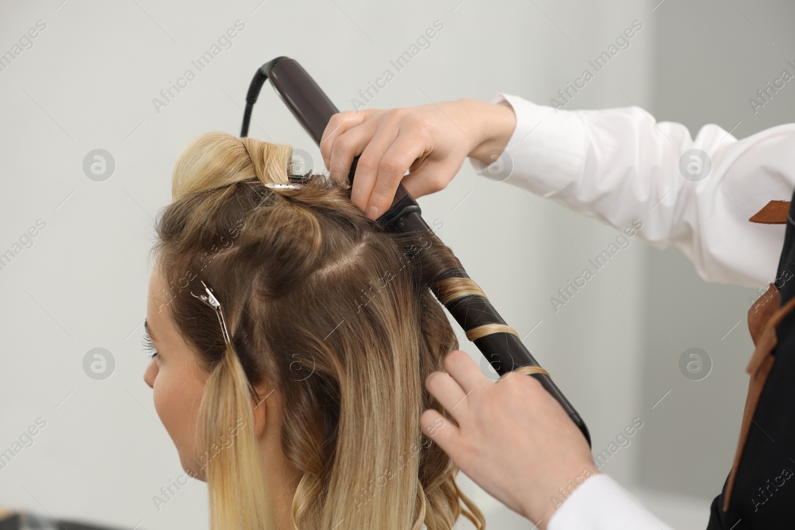 Photo of Hair styling. Hairdresser curling woman's hair in salon, closeup