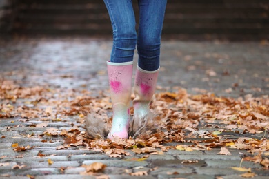 Photo of Woman wearing rubber boots splashing in puddle after rain, focus on legs. Autumn walk