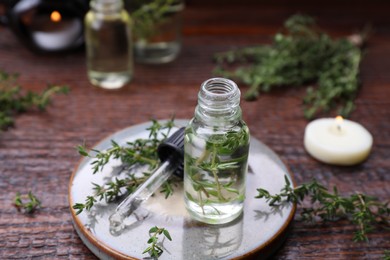 Photo of Thyme essential oil and fresh plant on wooden table, closeup