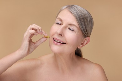 Beautiful woman taking vitamin capsule on beige background