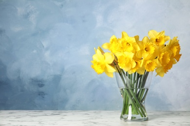 Bouquet of daffodils in vase on table against color background, space for text. Fresh spring flowers