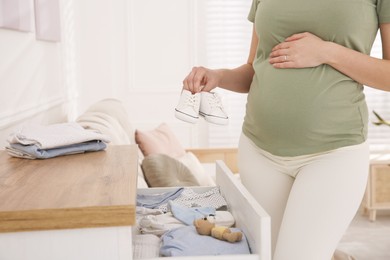 Photo of Pregnant woman holding baby booties at home, closeup