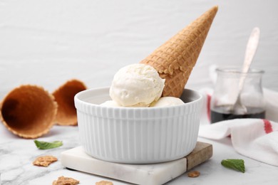 Photo of Scoops of ice cream with caramel sauce and wafer cone on white marble table, closeup