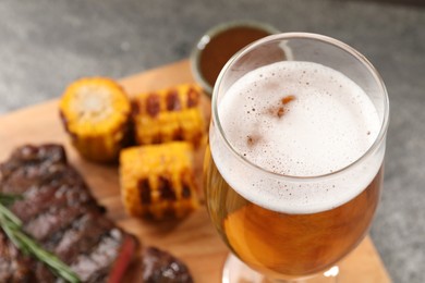 Photo of Glass of beer, delicious fried steak and corn on grey table, closeup. Space for text
