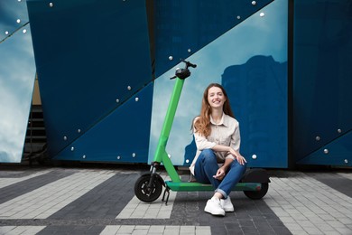 Photo of Happy woman sitting on modern electric kick scooter on city street, space for text