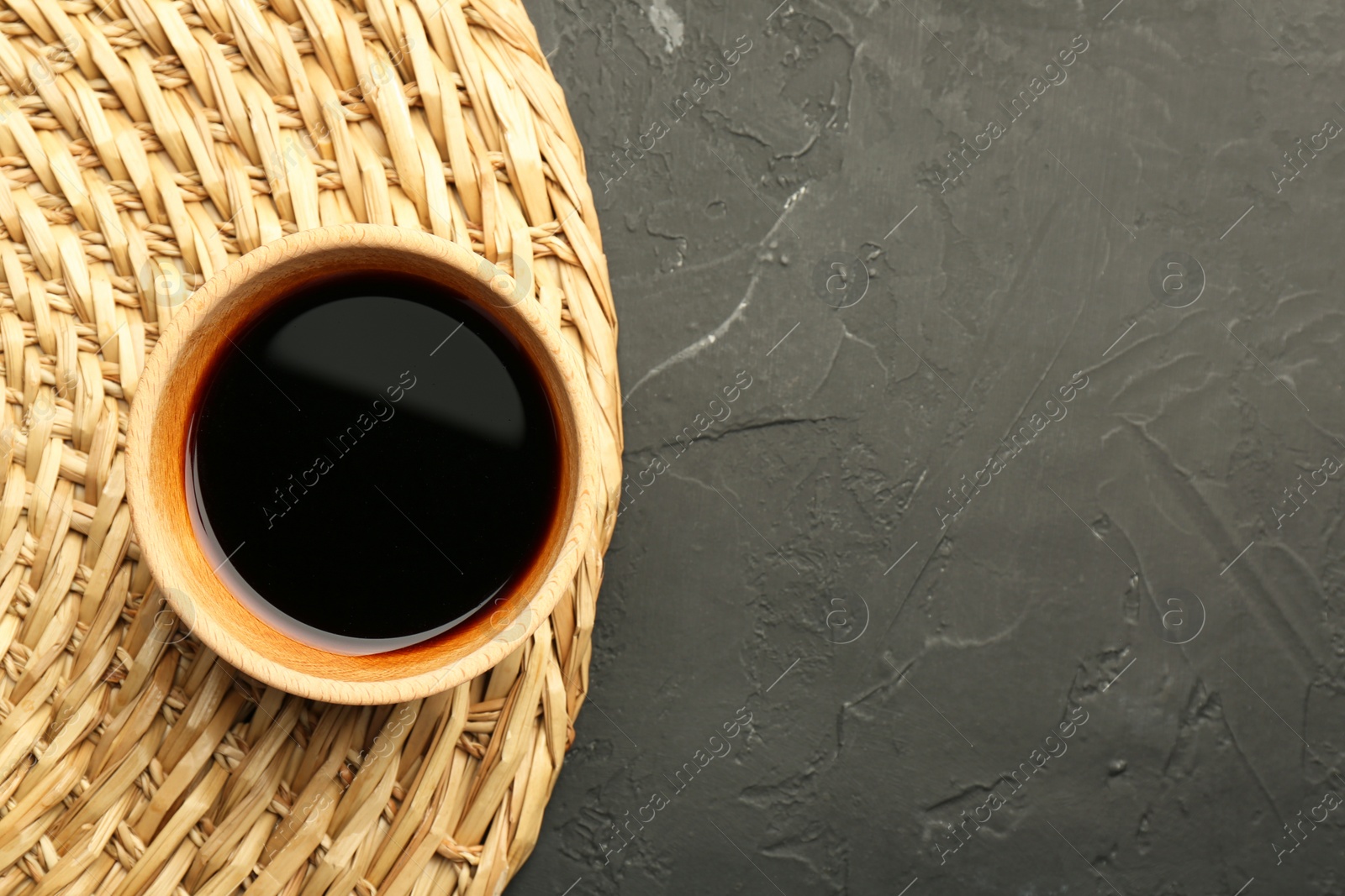 Photo of Soy sauce in bowl on black textured table, top view. Space for text