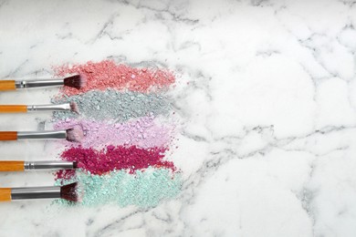 Photo of Makeup brushes and scattered eye shadows on white marble table, flat lay. Space for text