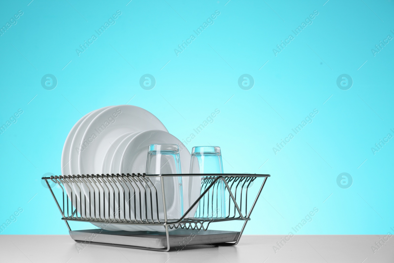 Photo of Drying rack with clean dishes and glasses on table against color background. Space for text