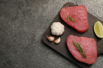 Raw tuna fillets with rosemary, lime and garlic on gray table, top view. Space for text