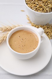 Photo of Cup of barley coffee, grains and spikes on white table, closeup