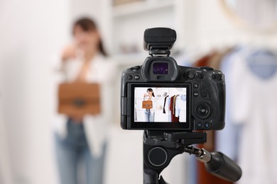 Photo of Fashion blogger showing her clothes while recording video at home, focus on camera