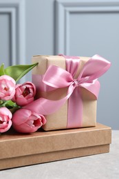 Beautiful gift box with bow and pink tulip flowers on light table