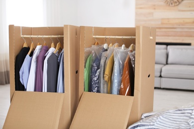 Photo of Cardboard wardrobe boxes with clothes on hangers in living room