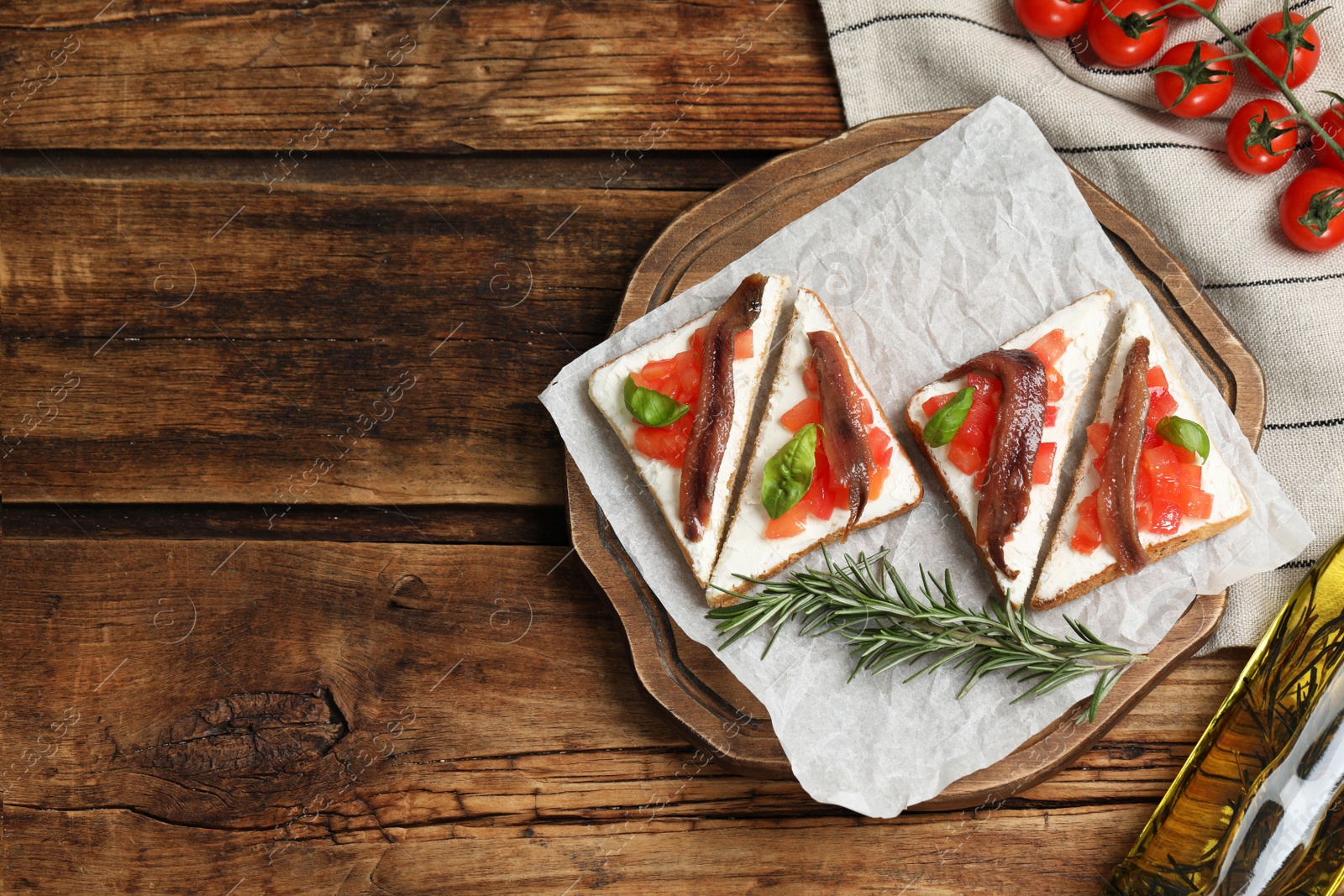 Photo of Delicious sandwiches with cream cheese, anchovies, tomatoes and basil on wooden table, flat lay. Space for text