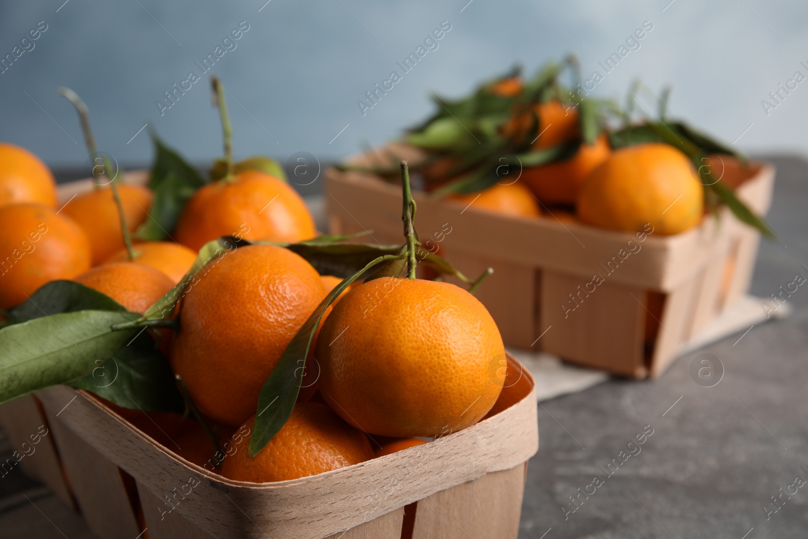 Photo of Fresh ripe tangerines with green leaves in crates on table