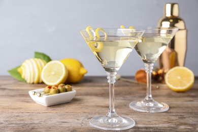 Photo of Glasses of lemon drop martini cocktail with zest on wooden table against grey background