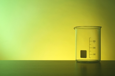 Photo of Empty beaker on table against color background. Chemistry laboratory glassware