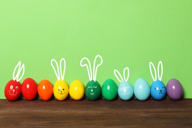 Several eggs with drawn faces and ears as Easter bunnies among others  on wooden table against green background