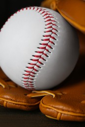 Photo of Leather baseball glove with ball on wooden table, closeup
