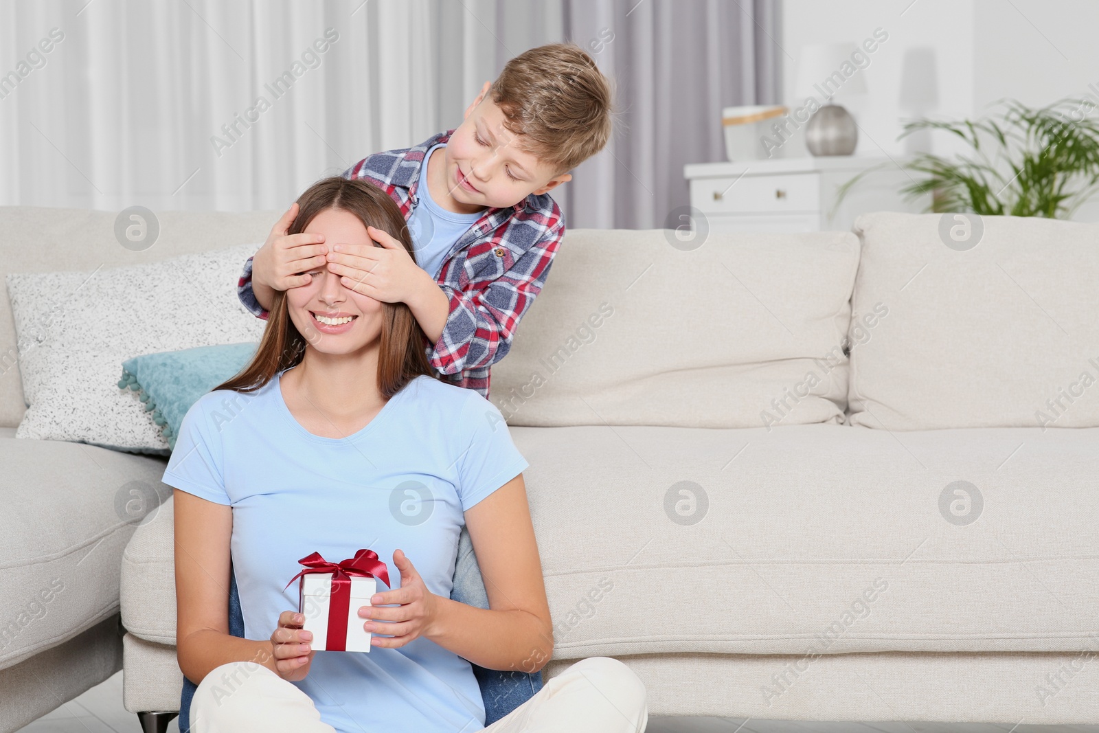 Photo of Little boy presenting his mother with gift on sofa at home