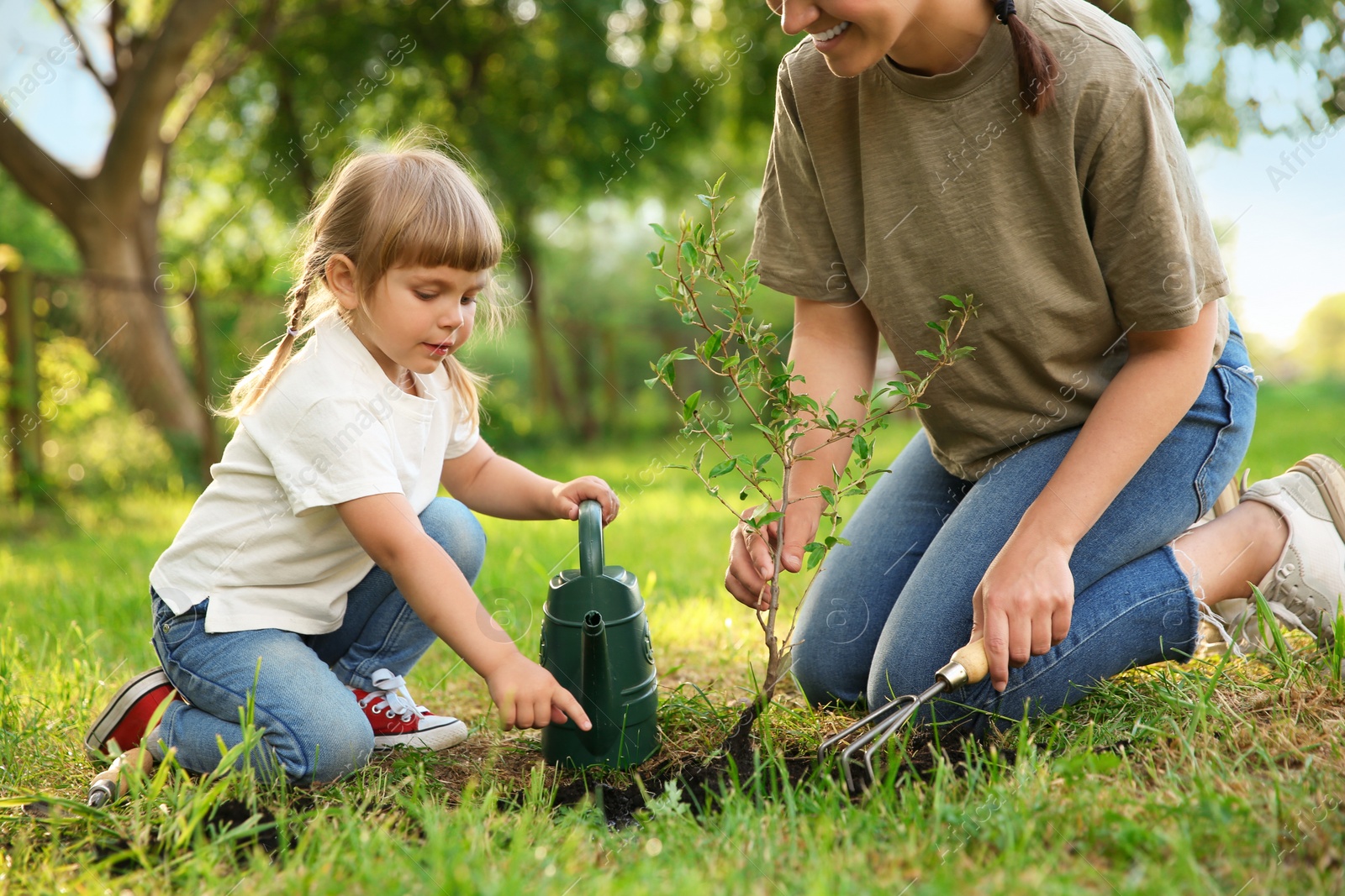 Photo of Mother and her daughter planting tree together in garden