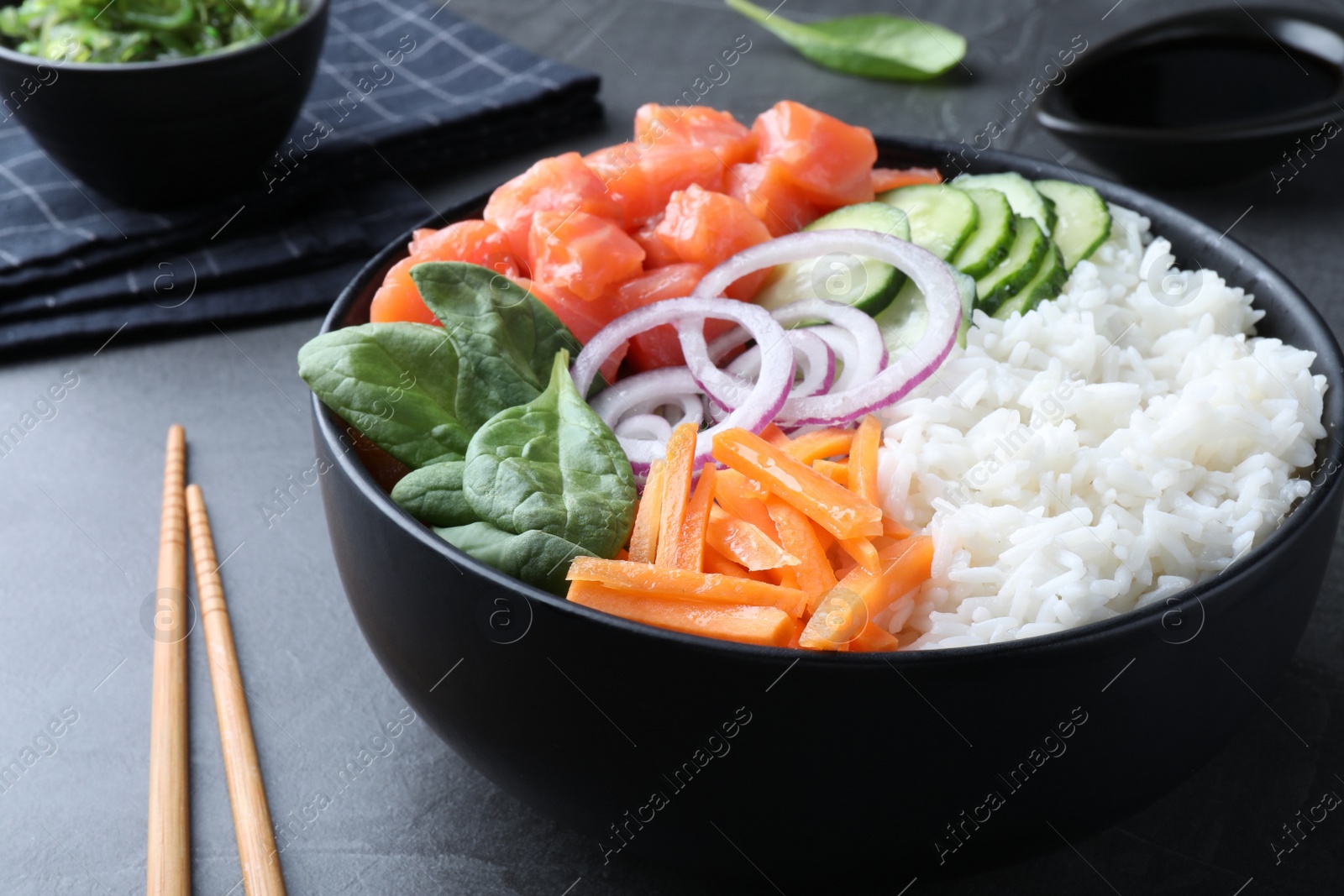 Photo of Delicious poke bowl with salmon and vegetables served on grey table, closeup