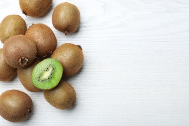 Photo of Cut and whole fresh kiwis on white wooden table, flat lay. Space for text