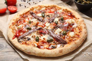 Tasty pizza with anchovies and ingredients on wooden table