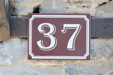 Plate with house number thirty seven on stone wall outdoors, closeup