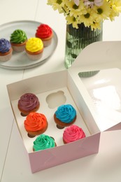 Photo of Delicious colorful cupcakes and beautiful flowers on white table