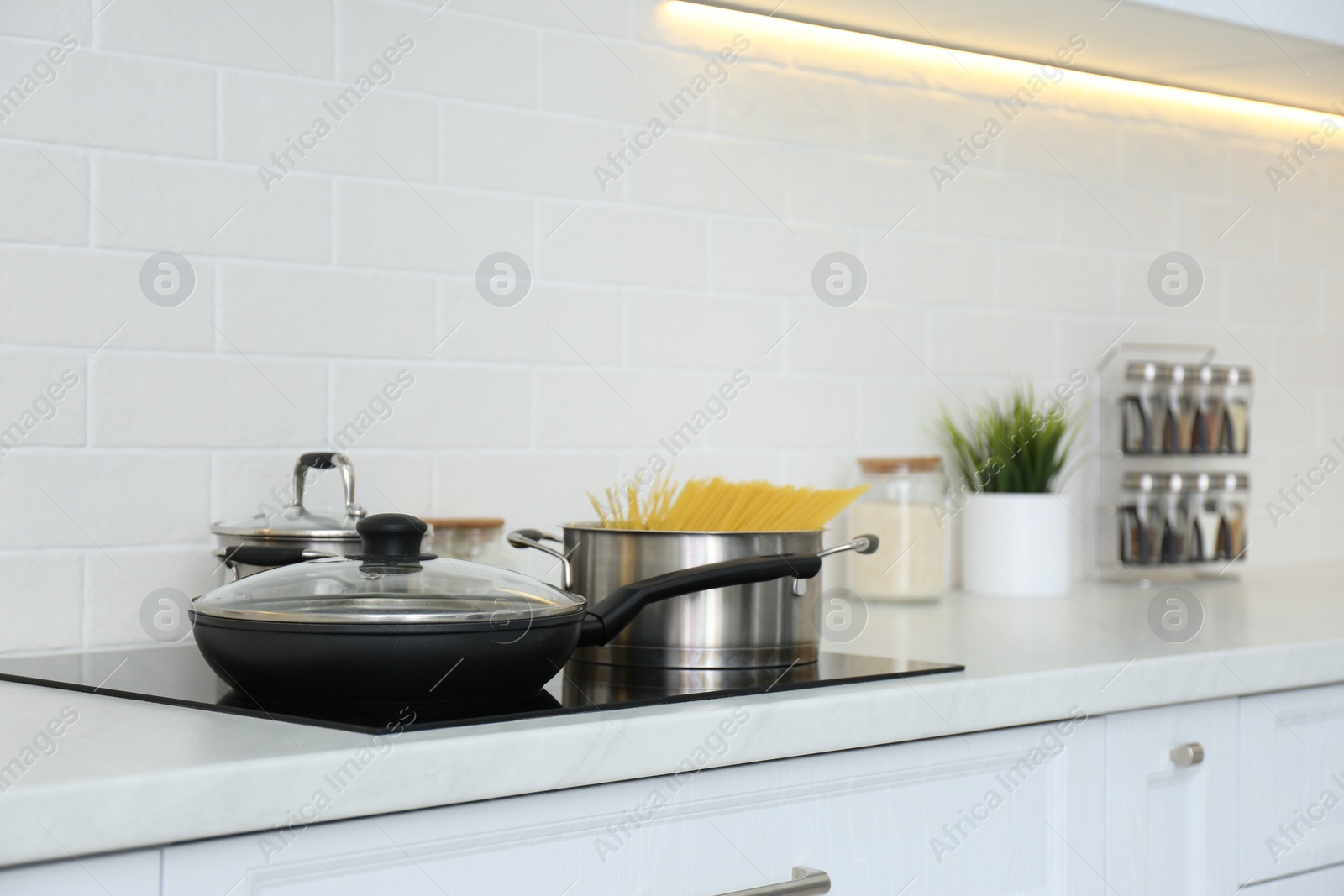 Photo of Pot with uncooked pasta and frying pan on stove in kitchen