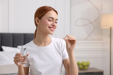 Photo of Happy young woman with pill and glass of water in room, space for text. Weight loss
