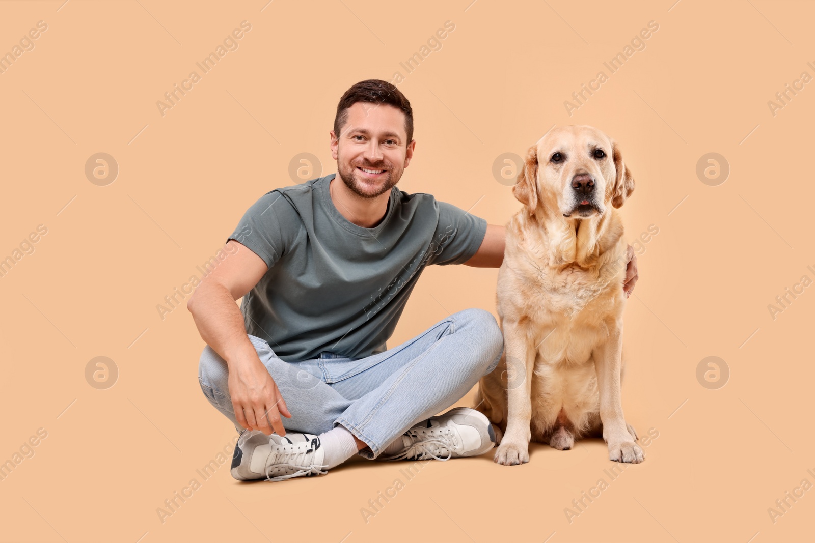 Photo of Man hugging with adorable Labrador Retriever dog on beige background. Lovely pet