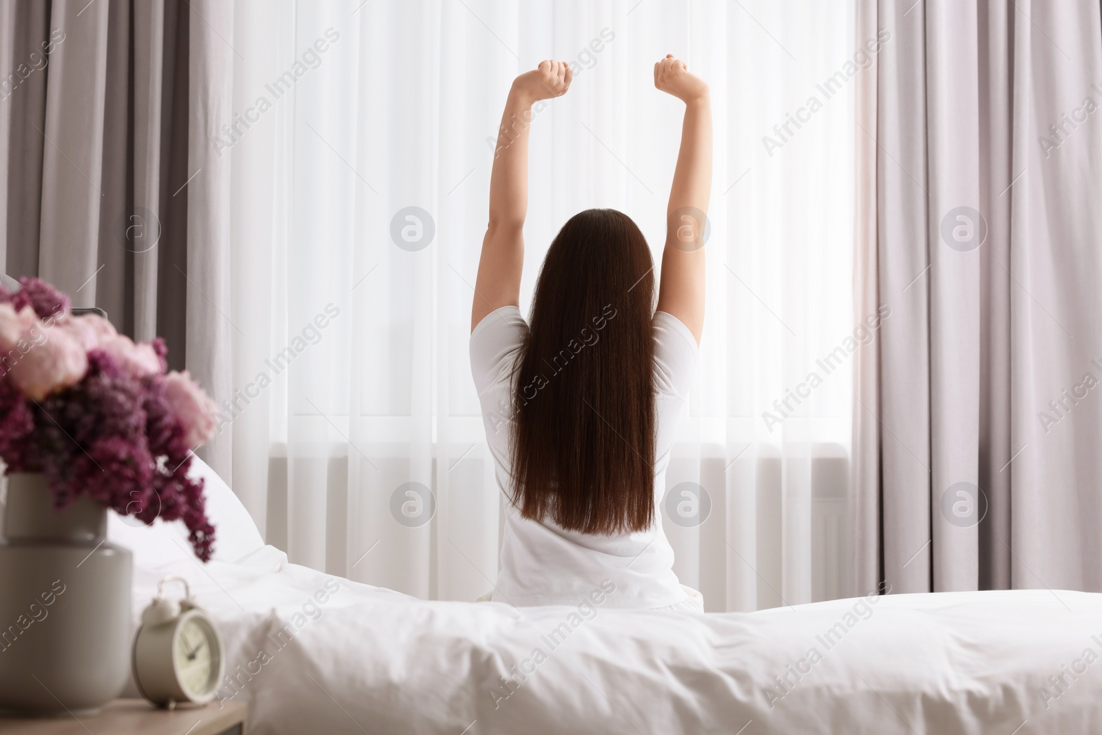 Photo of Woman stretching on bed at home, back view. Lazy morning