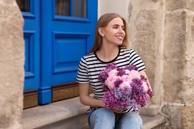 Beautiful woman with bouquet of spring flowers near building outdoors